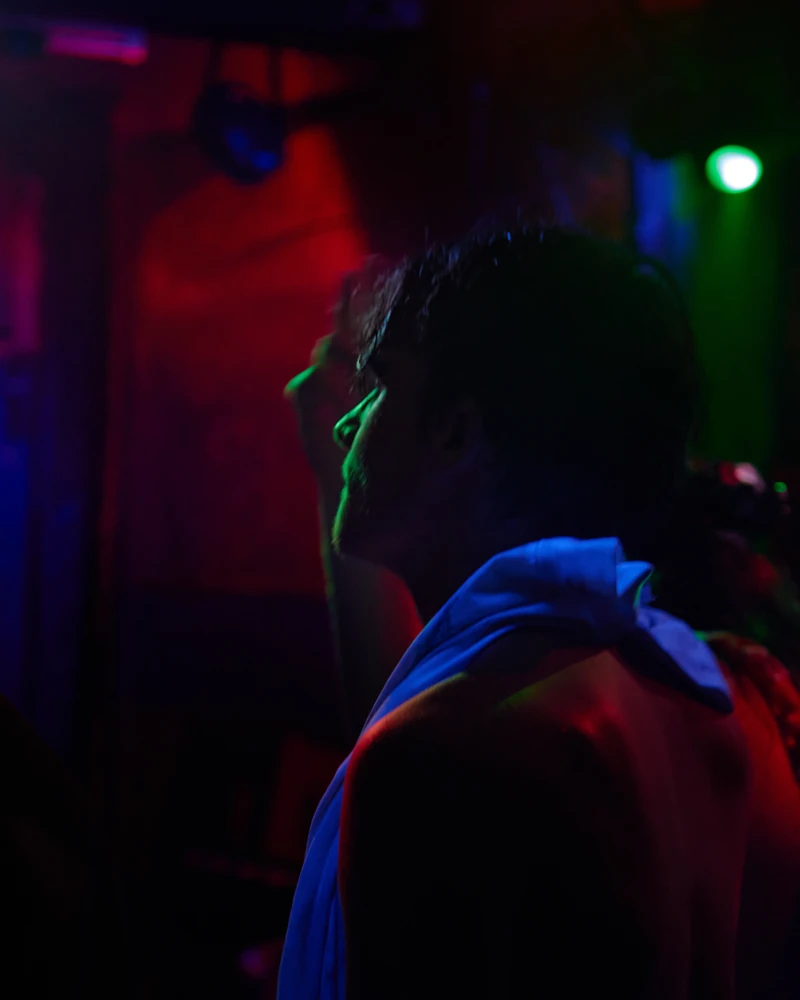 Portrait de profil dans la pénombre d'un club, éclairé de rouge, de bleu et de vert.