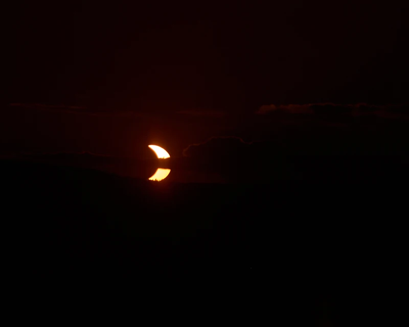 Éclipse partielle de Soleil : un fin croissant orangé dans un ciel presque noir.